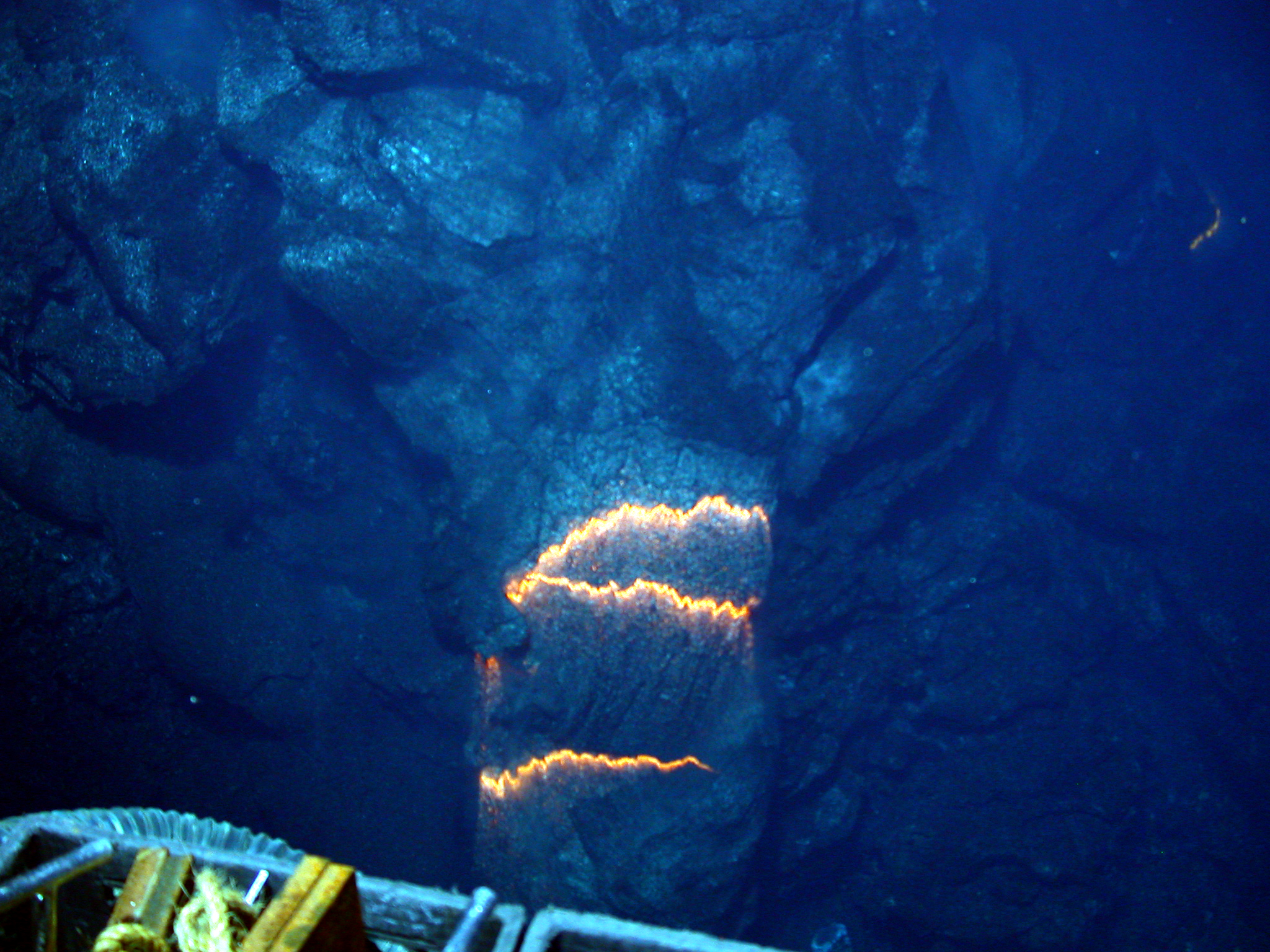 Bands of glowing magma, about 2,200 degrees Fahrenheit, are exposed as a pillow lava tube extrudes down slope from a submarine volcano. The image shows an approximately three-foot section across in an eruptive area spanning 100 yards and which runs...