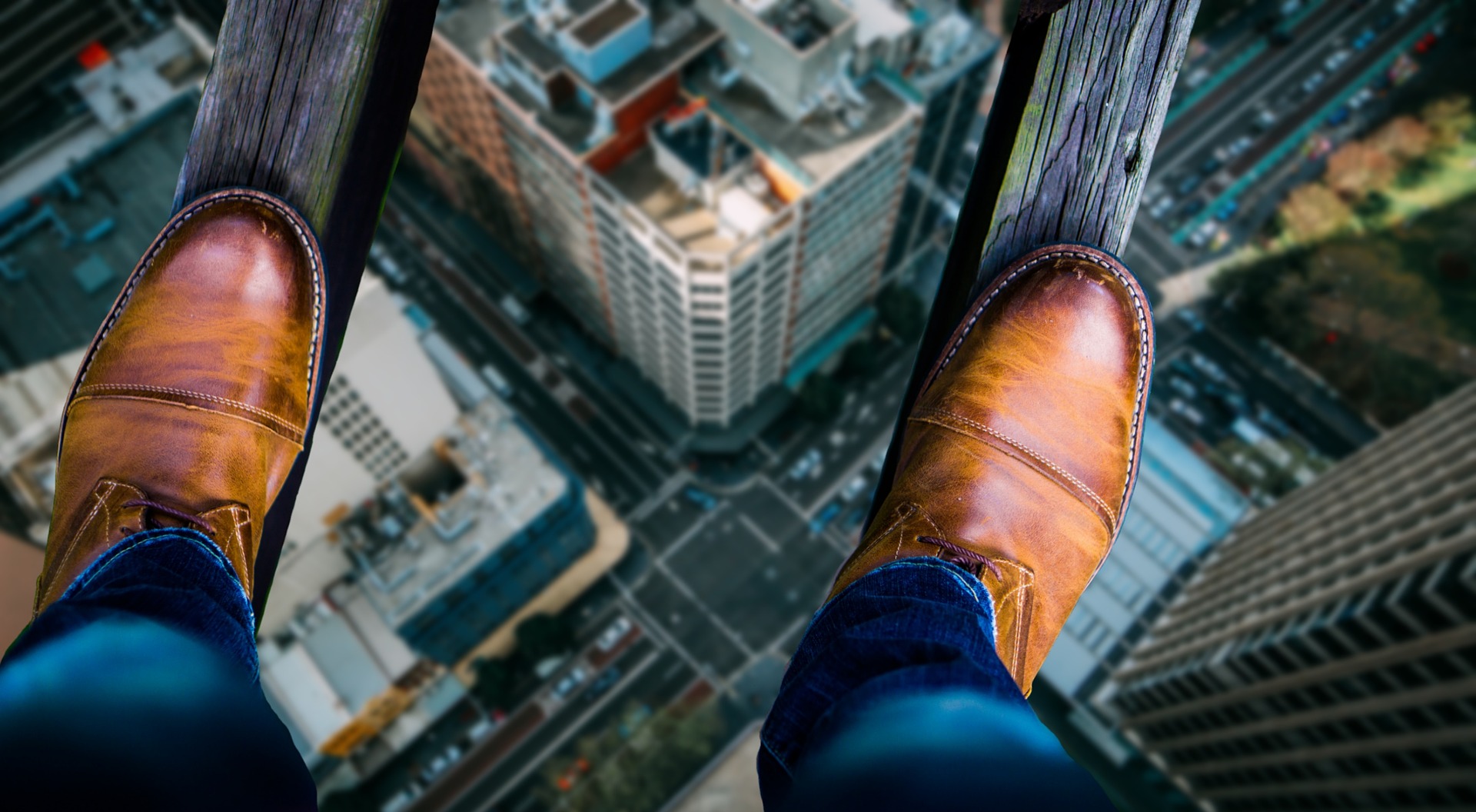 Looking down at a man's shoes as he stands on two thin wooden beams, high above a city street