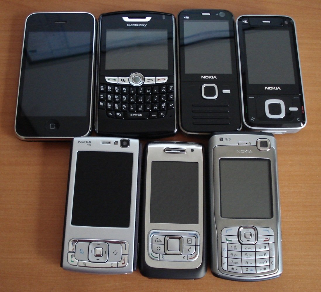 Assorted smartphones. From left to right, top row: iPhone 3G, Blackberry 8820, Nokia N78, Nokia N81, (bottom row) Nokia N95, Nokia E65, Nokia N70.