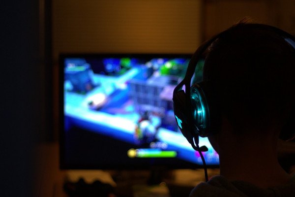 View of a person's head from behind with headphones on playing a video game.