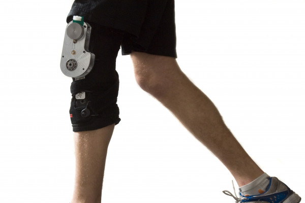 The biomechanical energy harvester comprises an aluminium chassis and generator (cylindrical component at the top of the chassis with green plastic attached) mounted on a customized orthopaedic knee brace (black), totalling 1.6 kg mass.