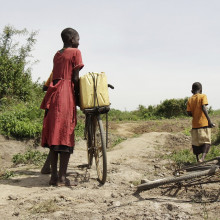 三个孩子在乌干达的一条土路上骑自行车。