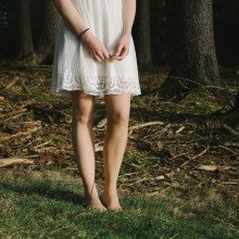 一个身穿白色连衣裙的女人站在森林里，腰部以下。