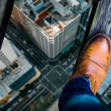 俯视一个男人的鞋子，他站在高高的城市街道上的两根细木梁上